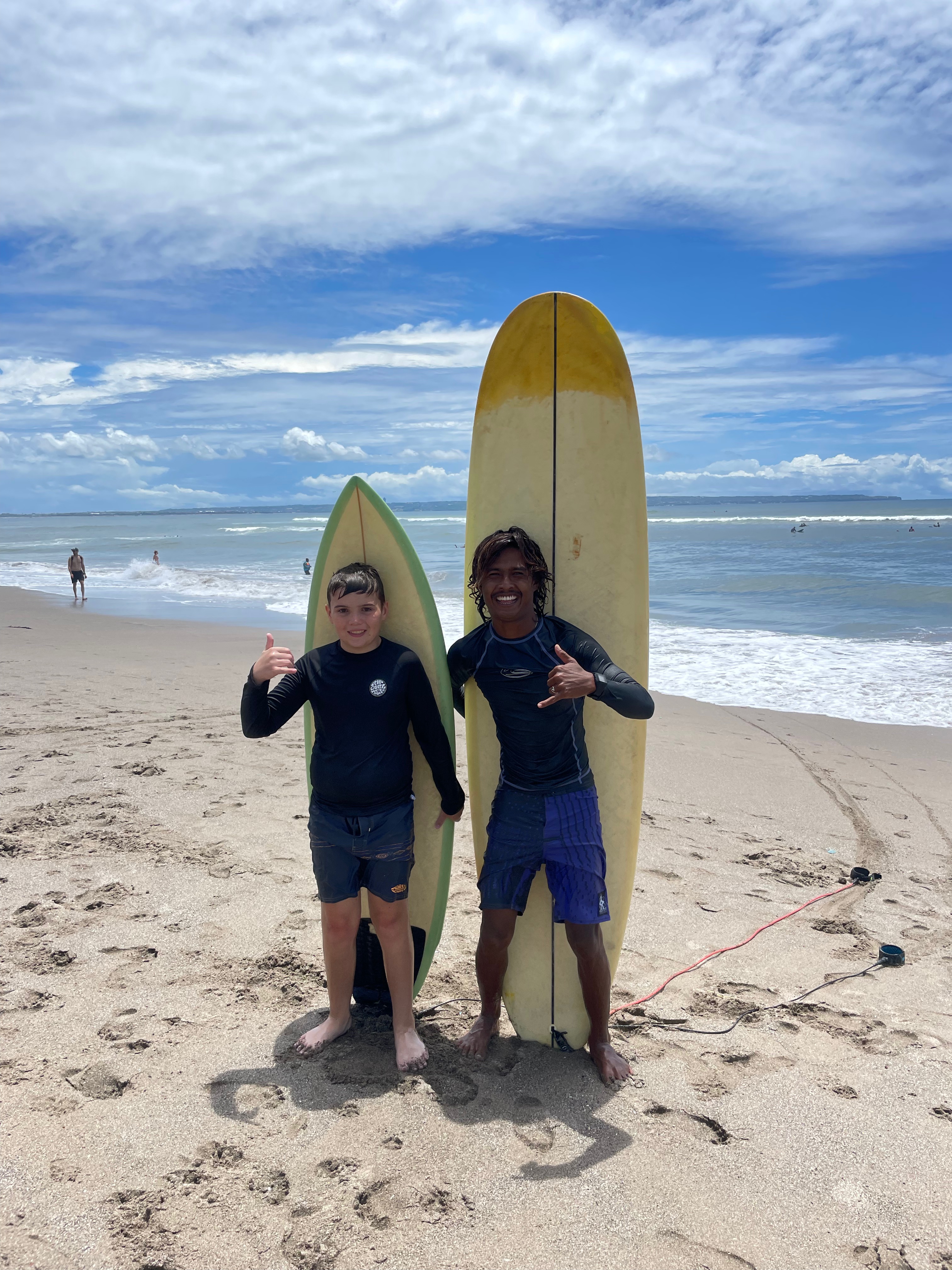 urf instructor and child smiling for a photo after a surf lesson, with a surfboard behind them and the ocean in the background.
