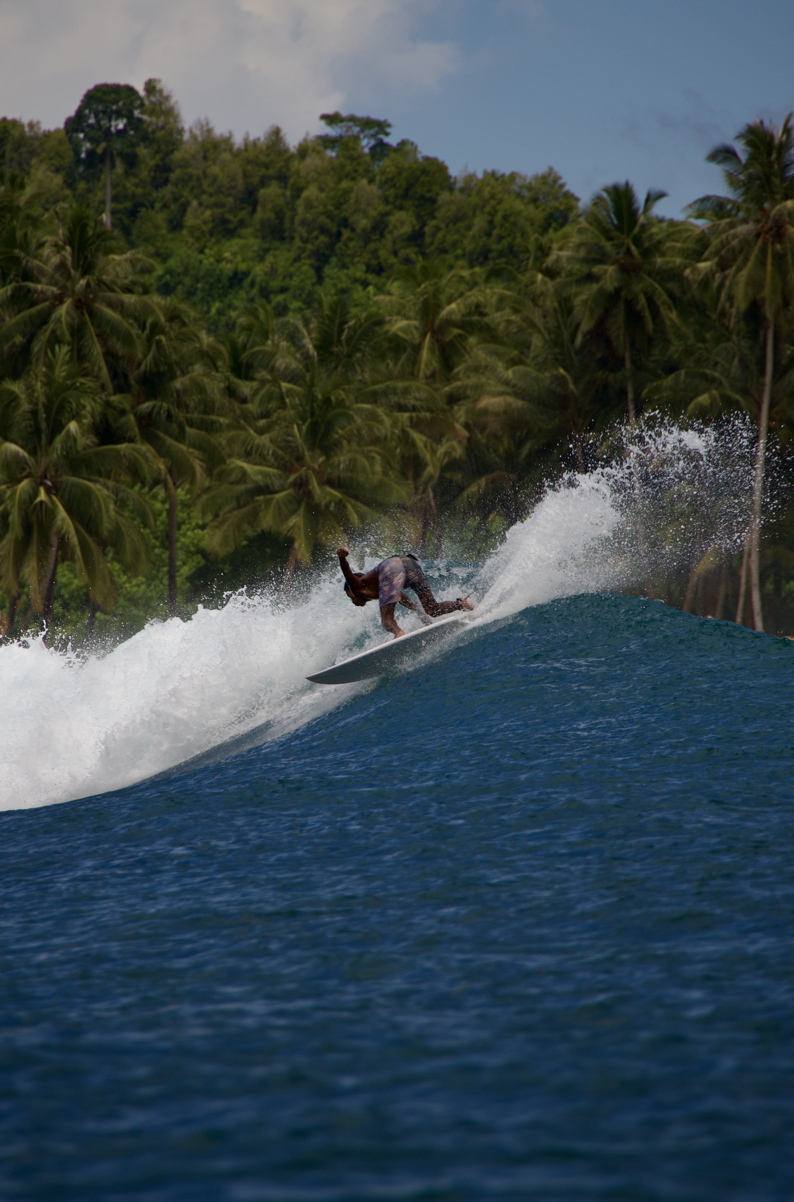 Surfer executing a backside turn on a wave in Bali, captured from the water with tropical palm trees in the background